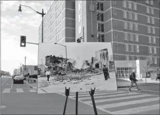  ?? PABLO MARTINEZ MONSIVAIS / AP ?? An April 6, 1968, photo of the smoldering remains of a building is placed on an easel as people walk at the corner of the present-day 7th and O streets in northwest Washington.