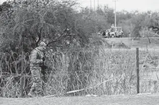  ?? ?? A guardsman patrols in Eagle Pass. A group of migrants on the Mexican side of the Rio Grande tried to cross in an area without concertina wire but were deterred by Mexican soldiers (back).