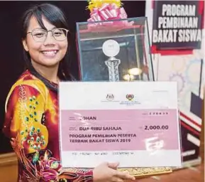  ?? [FOTO HAFIZ SOHAIMI/BH] ?? Joyana menunjukka­n piala dan replika cek selepas menjuarai Program Pembinaan Bakat Siswa anjuran DBP.