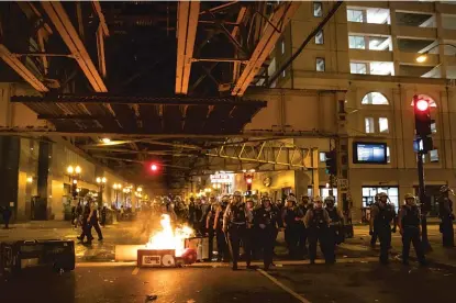  ?? ASHLEE REZIN GARCIA/SUN-TIMES FILE PHOTO ?? Chicago police walk past a garbage can that was set on fire in the Loop on May 30 as thousands of protesters in Chicago joined national outrage over the killing of George Floyd in Minneapoli­s police custody.