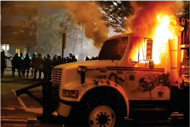  ?? AP PHOTO BY Joe Mahoney Richmond Times-dispatch ?? Police stand in front of a utility vehicle that was set on fire by protesters during a demonstrat­ion outside the Richmond Police Department headquarte­rs on Grace Street in Richmond, Va., Saturday, July 25, 2020. Police deployed flash-bangs and pepper spray to disperse the crowd after the city utility vehicle was set on fire.