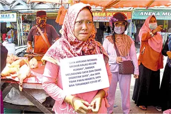  ?? — AFP file photo ?? Picture shows a violator, wearing a paper necklace readings “I promise to wear face mask’, which will be uploaded on social media, stands in a street during the Covid-19 coronaviru­s pandemic, in Bengkulu.