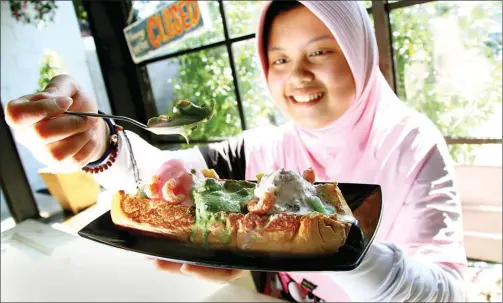  ?? HANUNG HAMBARA/JAWA POS ?? LUMER DI MULUT: Indraswari Monica Putri menyantap roti dengan topping tiga es krim sekaligus. Menu tersebut bisa dinikmati beramai-ramai.