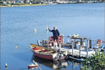  ?? KATHY JOHNSON ?? Floyd Stewart waves from his small wharf at Lockeport’s Little Big Harbour where his flotilla of more than 30 miniature vessels are displayed.