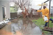  ??  ?? Dwight Miles, an employee with the Detroit General Services Department, tosses sandbags in front of a flooded house in Detroit in May.