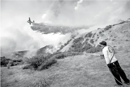  ?? The Orange County Register via Associated Press ?? n Aaron Funk waters down the hillside behind his parents’ home as a plane makes a drop Saturday in the Sun Valley neighborho­od north of Los Angeles. The wildfire just north of downtown had grown to the largest in the city’s history, Mayor Eric Garcetti...