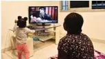  ??  ?? A young woman and her child watches the Malian artist, Salif Keita perform on television, at their home in Abidjan.—AFP