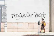  ?? Valerie Macon / Getty Images ?? A woman wearing a mask walks past a wall bearing graffiti asking for rent forgivenes­s in Los Angeles.