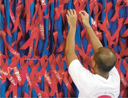  ?? AFP PIC ?? A volunteer pinning ribbons bearing the names of people who died of HIV/AIDS at a memorial service in Singapore.