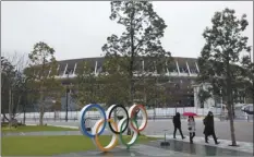  ?? AP file photo ?? People walk past the Olympic rings near the New National Stadium in Tokyo on March 4. Repercussi­ons of cancelling the Tokyo Olympics would reach into every corner of the globe.