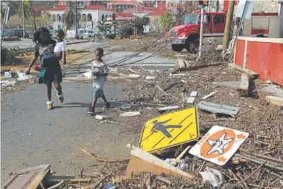  ?? Press Ricardo Arduengo, The Associated ?? A woman and her children walk past debris left by Hurricane Irma in Charlotte Amalie, St. Thomas, in the U.S. Virgin Islands, on Sept. 10. Two weeks later, the islands were ravaged again by Hurricane Maria.