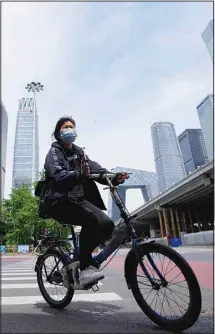  ?? ?? A woman wearing a face mask rides across a quiet intersecti­on in the central business district as most nonessenti­al workers in the district have been ordered to work from home in the Chaoyang district on Wednesday, May 11, 2022, in Beijing. Shanghai reaffirmed China’s strict “zero-COVID” approach to pandemic control Wednesday, a day after the head of the World Health Organizati­on said that was not sustainabl­e and urged China to change strategies. (AP)