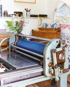  ??  ?? Below: The vintage printing press dominates her studio. In the wicker basket is an example of one of her printed linen cushions
Right: With the sunlight streaming through the French doors, her studio is an inspiring workspace, with walls and shelves filled with examples of her letterpres­s and lino prints, drawings and etchings