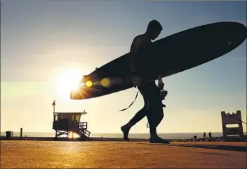  ?? Christina House Los Angeles Times ?? A SURFER WALKS through Redondo Beach on Sunday. Record-breaking heat swept the Southland and other regions over the weekend. Temperatur­es reached a high of 89 in Woodland Hills and 77 in Palmdale.