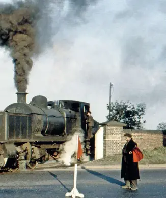  ?? COLOUR RAIL ?? William Francis negotiates the infamous level crossing over the A5 trunk road near Atherstone on November 7 1960. The cottages on the left are still extant, as is the wall on the right.