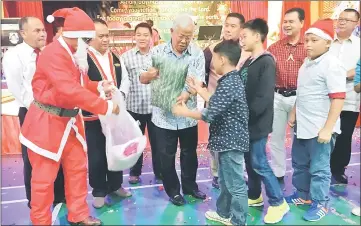  ??  ?? Manyin (centre) presents a gift from the organisers to these children. From right are Dahim, Ik Pahon, John, Father Jerome Juleng, Henry and Boniface.