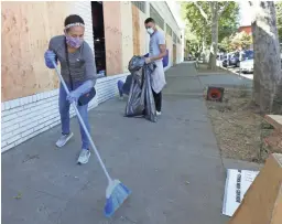  ??  ?? Volunteer Jennifer Kistler-McCoy sweeps up glass Monday from store windows shattered Sunday in Sacramento, Calif.