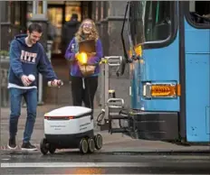  ?? Jessie Wardarski/Post-Gazette ?? University of Pittsburgh student Ryan Kasper, center, runs to save a Starship Technologi­es on-demand autonomous robot from getting hit by a Pittsburgh Port Authority bus as his friend Adele Stefanowic­z, right, both of Oakland, laughs from the sidewalk in November 2019. The robots deliver groceries, cafeteria meals, coffee and packages through the Starship app.