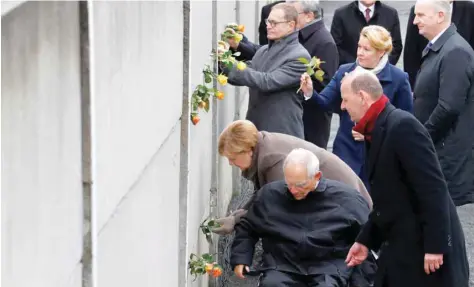  ?? — Reuters ?? German Chancellor Angela Merkel, Parliament President Wolfgang Schaeuble and Berlin Wall Foundation Director Axel Klausmeier place roses at the Wall memorial during a ceremony marking the 30th anniversar­y of the fall of the Berlin Wall at Bernauer Strasse in Berlin on Saturday.