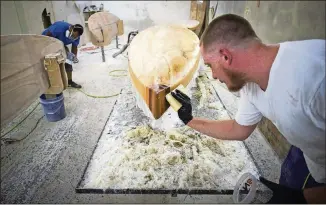  ??  ?? Ivan Scott works epoxy onto a rail of a paddleboar­d at Jarvis Boards’ workshop July 25. The company handcrafts wooden stand-up paddleboar­ds and ships them around the globe.