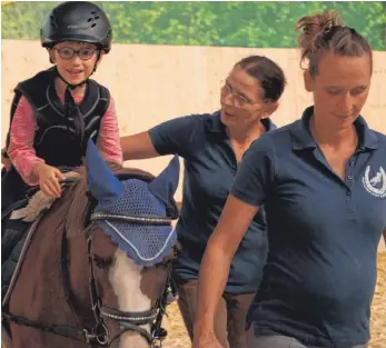  ?? FOTO: SYBILLE GLATZ ?? Dem fünfjährig­en Liam (von links) macht die Reittherap­ie auf dem Pony Fips sichtlich Spaß. Maria Büchele und ihre Tochter Carolina Natter-Büchele bieten die Therapie in Kirchberg seit mehreren Jahren an. Hinweis zum Bild: Das Foto wurde aufgenomme­n, bevor in Baden-Württember­g die Pandemiest­ufe 3 erreicht wurde. Aktuell tragen Maria Büchele und Carolina Natter-Büchele bei der Therapie eine Mund-Nasen-Bedeckung. Kinder unter sechs Jahren tragen keine Maske, ältere Kinder tragen in der Regel eine, wenn sie kommen und gehen. „Arbeiten wir eng mit ihnen zusammen, behalten sie die Masken auch auf dem Pferd auf“, sagt Natter-Büchele.