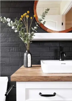  ??  ?? La céramique à surface irrégulièr­e est une tendance artisanale très forte en ce moment. La texture créée par ces carreaux charbonneu­x entre en résonance avec le style champêtre du meuble-lavabo mouluré et du comptoir à effet bois.