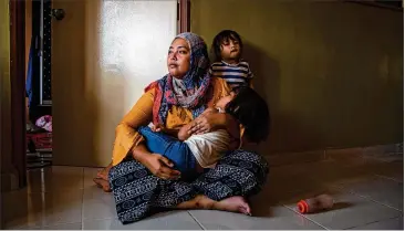  ??  ?? Siti Noor Azila, the second wife of Che Abdul Karim Che Abdul Hamid, sits with her two daughters in her family’s home in Gua Musang, Malaysia. Siti Noor’s husband, a 41-year- old man, married an 11-year- old girl.
