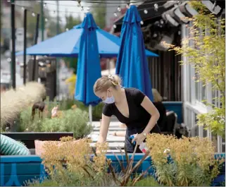  ?? The Canadian Press ?? A server wears a face mask while cleaning a table on the patio at an Earls restaurant in Vancouver. B.C. began phase two of the reopening of its economy, allowing certain businesses that were ordered closed due to COVID-19 to open their doors to customers if new health and safety regulation­s are followed.