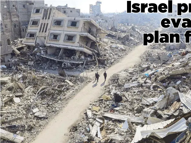  ?? REUTERS ?? Palestinia­ns walk past destroyed houses in the Jabalia refugee camp in northern Gaza Strip on Sunday, amid the ongoing war between Israel and Hamas.