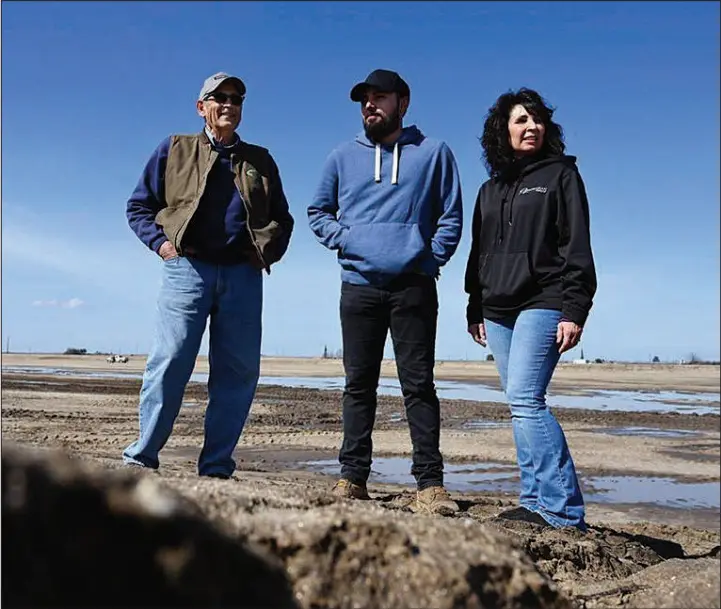  ?? TNS ?? Jennifer Peters of Markarian Family LP, right, with Robert Markarian, left, and Kevin Markarian, center, representi­ng three generation­s, stand on March 3 along the edge of a 20-acre basin on their land that the family’s business in California’s Central Valley has dedicated to a National Resources Conservati­on Service project in hopes of recharging the local aquifer.