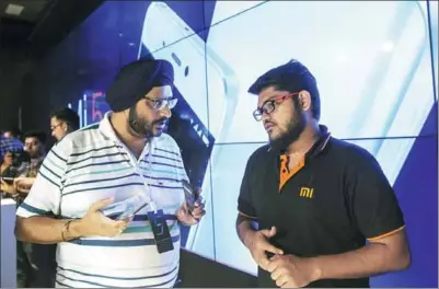  ?? BLOOMBERG ?? An attendee (left) speaks to a representa­tive at the launch of the Xiaomi Corp MI 5 smartphone in New Delhi. Foxconn Technology Group began assembling Xiaomi’s first made-in-India smartphone from a new plant in the country.