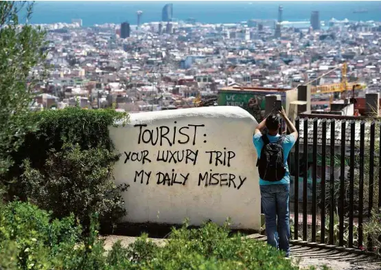  ?? Josep Lago - 10.ago.2017/AFP ?? Turistas tira foto do panorama de Barcelona ao lado de pixação crítica ao fluxo de visitantes na cidade: “sua viagem de luxo minha miséria diária”