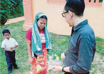  ??  ?? SEORANG guru menyambut murid Orang Asli di pintu pagar masuk SK Tohoi sambil menghulurk­an coklat untuk menarik minat murid ke sekolah.