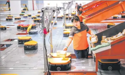  ?? XINHUA ?? Employees of a delivery service company use robots to sort parcels in Yiwu, Zhejiang province.
