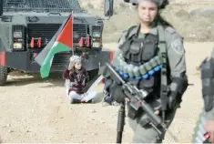  ?? Reuters ?? A girl holding a Palestinia­n flag sits on the ground as an Israeli border policewoma­n stands guard during a protest against the Israeli barrier in the West Bank village of Bilin near Ramallah, recently. —