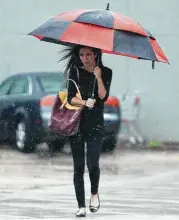  ?? Elizabeth Conley / Houston Chronicle ?? A pedestrian holds on to her umbrella as the wind picks up downtown Friday. Officials say Harvey’s primary threat will be flooding rather than wind.