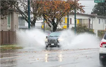  ?? FRANCIS GEORGIAN ?? A pickup truck drives through puddles in Vancouver. Temperatur­e records fell on Wednesday along with rain. The downpour triggered at least two mudslides and spurred the closure of a highway near Hope.