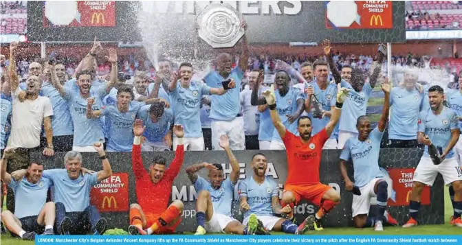  ??  ?? LONDON: Manchester City’s Belgian defender Vincent Kompany lifts up the FA Community Shield as Manchester City players celebrate their victory on the pitch after the English FA Community Shield football match between Chelsea and Manchester City at Wembley Stadium in north London yesterday. — AFP