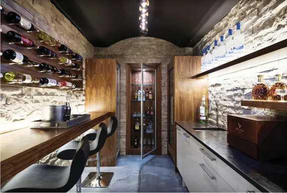  ??  ?? Concrete floors soften chiseled-edge ledge stone in the wine room where a barrel-vaulted ceiling overlooks high-gloss cabinetry and millwork details.