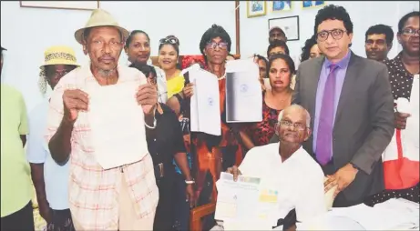  ??  ?? Some of the aggrieved villagers holding up the transport for the land they are presently occupying. Also in the photograph is their attorney Anil Nandlall (third from right).