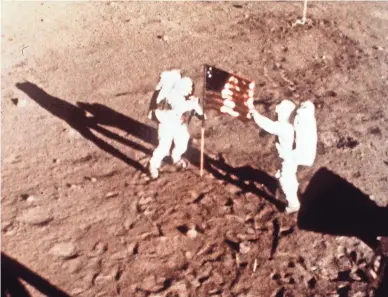  ?? NASA ?? Apollo 11 astronauts Neil Armstrong and Edwin E. “Buzz” Aldrin, the first men to land on the moon, plant the U.S. flag on the lunar surface on July 20, 1969. This photo was made by a 16mm movie camera inside the lunar module, shooting at one frame per second.