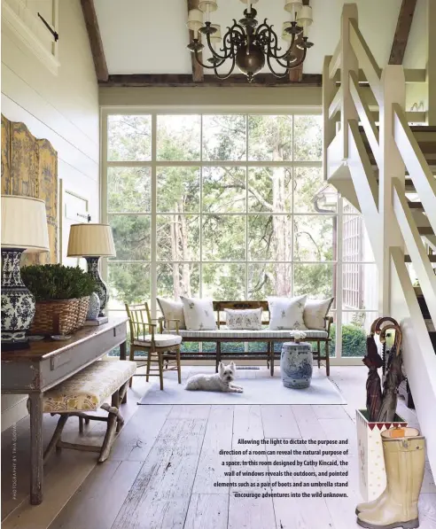  ??  ?? Allowing the light to dictate the purpose and direction of a room can reveal the natural purpose of a space. In this room designed by Cathy Kincaid, the wall of windows reveals the outdoors, and pointed elements such as a pair of boots and an umbrella stand
encourage adventures into the wild unknown.