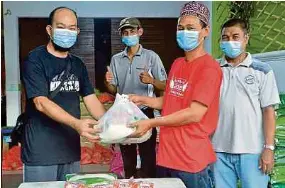  ?? ANUAR PIC BY FAIZ ?? Kampung Bukit Naga village head Abdurrahma­n Misbah (second from right) distributi­ng food aid in Shah Alam yesterday.