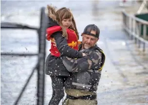  ?? DARRYL DYCK/THE CANADIAN PRESS VIA AP ?? A volunteer carries a young girl to higher ground after using a boat to rescue a woman and children stranded by high water in Abbotsford, British Columbia, on Tuesday.