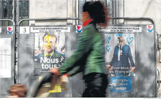  ?? MOHAMMED BADRA / EFE ?? Una mujer camina delante de carteles electorale­s de Emmanuel Macron y Marine Le Pen, ayer en una calle de París.