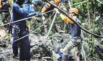  ?? — AFP photo ?? Thai rescue specialist­s (in orange) help a Thai Airforce soldier descent into a possible opening to the Tham Luang cave.