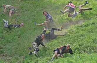  ?? PHOTOS BY KIN CHEUNG/THE ASSOCIATED PRESS ?? Participan­ts take tumbles competing in the men’s downhill race during the Cheese Rolling contest Monday at Cooper’s Hill in Brockworth, Gloucester­shire, England.