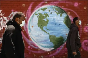  ?? MATT ROURKE - ASSOCIATED PRESS ?? In this April 22 file photo, people wearing a protective face mask as a precaution against the coronaviru­s walk past a mural of the world in Philadelph­ia.