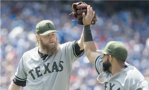  ?? CHRIS YOUNG / THE CANADIAN PRESS ?? Texas pitcher Andrew Cashner high-fives second baseman Rougned Odor during Sunday’s game at Rogers Centre in Toronto. Cashner pitched five-hit ball over seven innings as the Rangers salvaged the third game of the series with a 3-1 win Sunday.