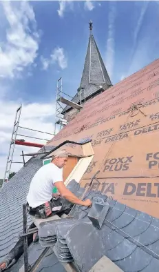  ?? RP-FOTO: ACHIM BLAZY ?? Arbeiten in luftiger Höhe: Dachdecker Martin Schauerte verlegt neue Naturschie­ferplatten auf dem Dach der Evangelisc­hen Stadtkirch­e. Dabei ist viel Handwerksk­unst gefragt.
